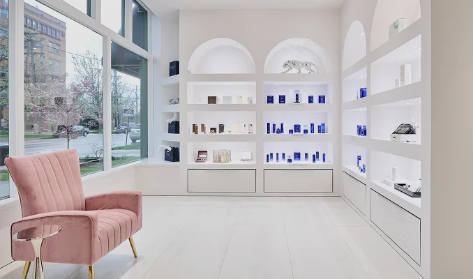 Modern minimalist retail boutique interior with white shelving, pink velvet chairs, and luxury product displays