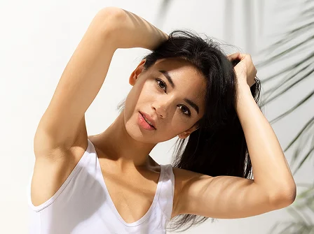 Woman with dark hair styling her hair while wearing white tank top against light background - hair In Cleveland, OH