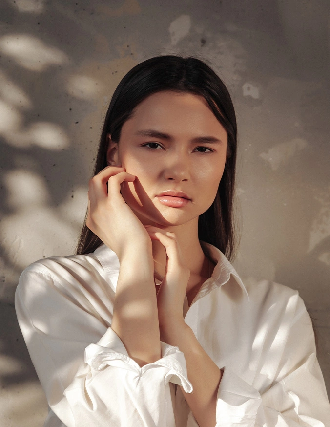 Young woman in white shirt posing thoughtfully with hand near face in soft natural lighting - Dermaplaning In Cleveland, OH